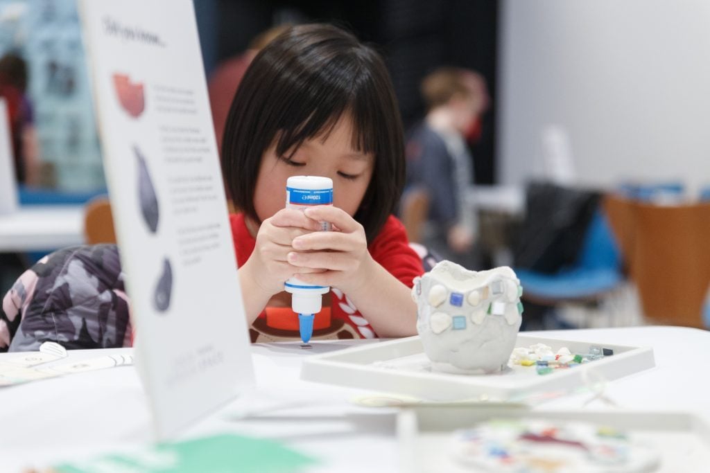 A young girl gluing tiles onto a clay pot at a craft workshop, one of many things to do with kids in London