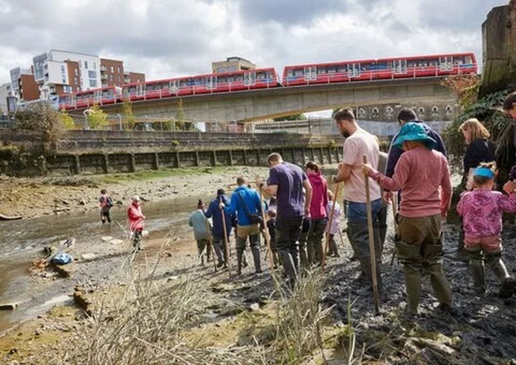 Families mudlarking on the Thames foreshore below a DLR line, one of many things to do with kids in London